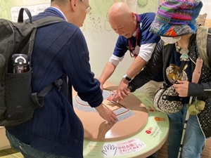 写真1 前方後円墳の模型を触る手を導きながら説明される学芸員さん